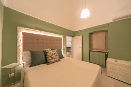 Camera da letto matrimoniale trullo Alfieri, con specchiera, sgabello, comò, finestra a muro, climatizzatore e termosifone.