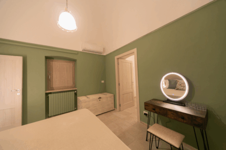 Camera da letto matrimoniale trullo Alfieri, con specchiera, sgabello, comò, finestra a muro, climatizzatore e termosifone.