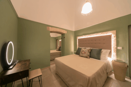 Camera da letto matrimoniale trullo Alfieri, con specchiera, sgabello, comò, finestra a muro, specchio, climatizzatore e termosifone.