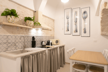 Cucina abitabile trullo Alfieri con diversi accessori: piano cottura ad induzione, lavabo, bollitore, macchina per il caffe, tavoli e sedie.
