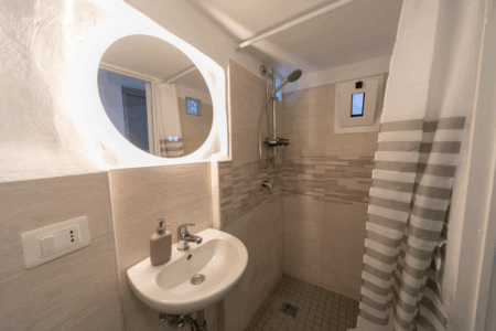 Altro bagno del trullo Alfieri con lavandino, bidet, doccia a muro con tendina. Ambiente dai toni neutri e rilassanti.