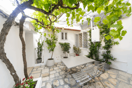 Esterno trullo Alfieri con tavoli e sedie, circondato da piante di viti e pavimentazione in pietra.