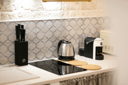 Dettaglio cucina abitabile trullo Alfieri con diversi accessori: piano cottura ad induzione, lavabo, bollitore, macchina per il caffe, tavoli e sedie.