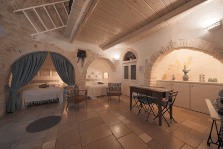 Vista trullo Artemis con due letti matrimoniali, tavoli e sedie, finestra a muro.