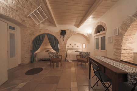 Vista trullo Artemis con due letti matrimoniali, tavoli e sedie, finestra a muro.