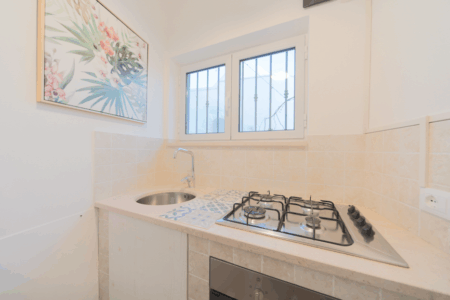 Cucina ad angolo del trullo Artemis. Con lavabo, piano cottura quattro fuochi e finestra che porta all'esterno.